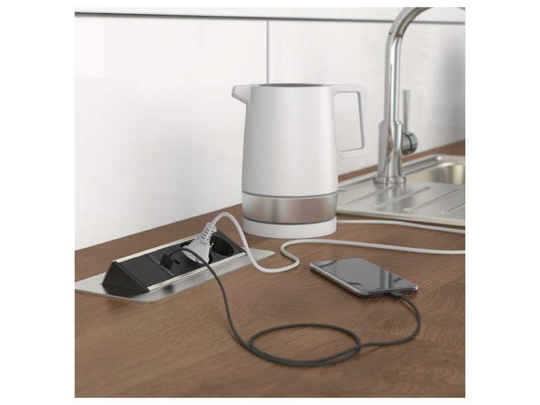 Een witte waterkoker en een smartphone worden opgeladen via een stopcontact in een keuken.