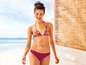 Een vrouw in een roze bikini met een tropische print staat op het strand.