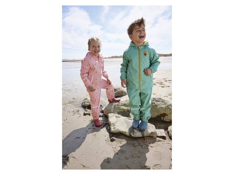 Deux enfants portent des vêtements de pluie sur la plage.