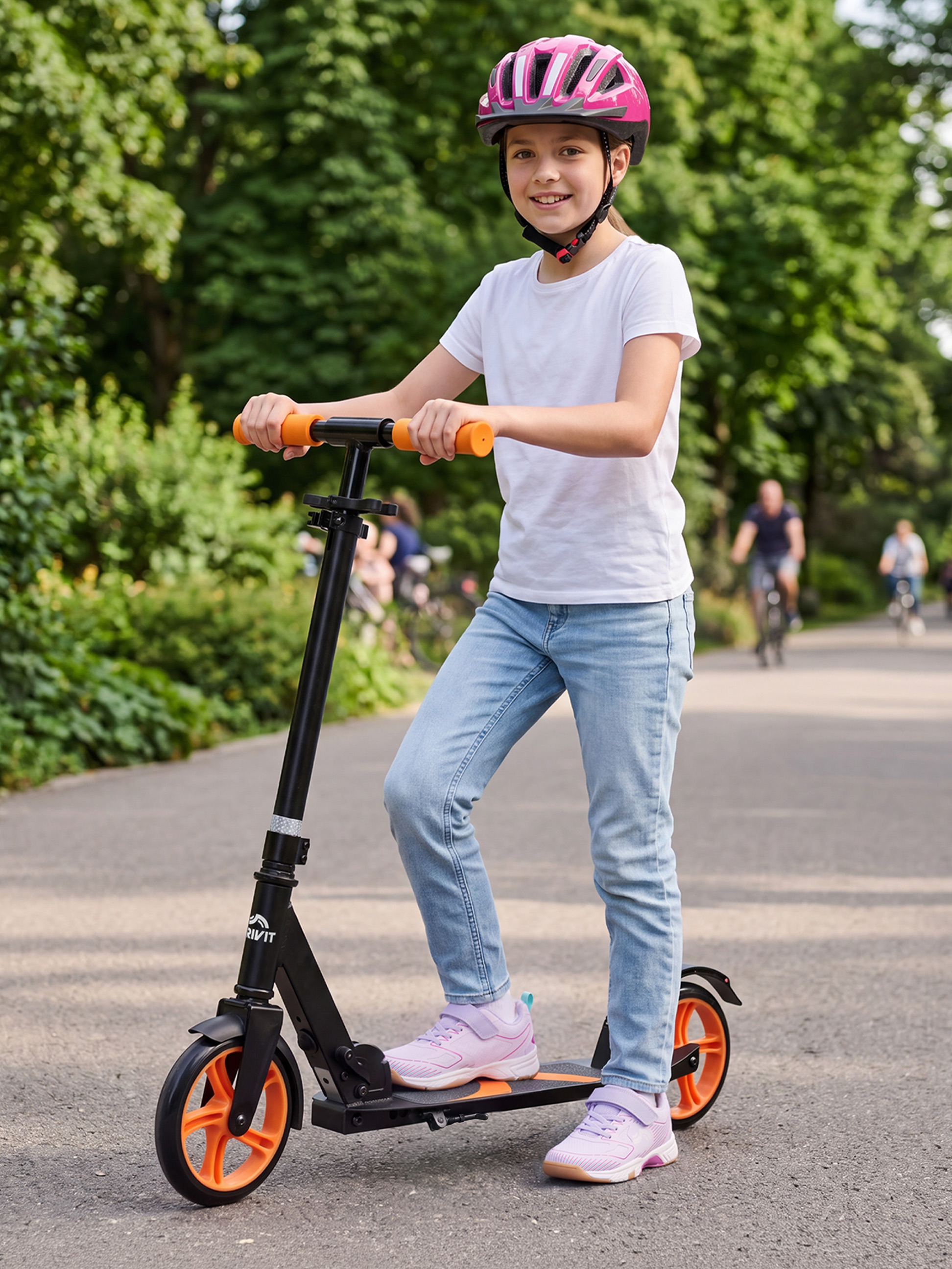 Fille avec un casque rose et une trottinette noire à roues oranges dans un parc.