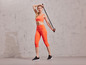 Vrouw in oranje sportbeha en leggings met een weerstandsband.