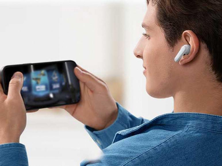 Homme en chemise en jean joue sur smartphone, portant un écouteur intra-auriculaire blanc.