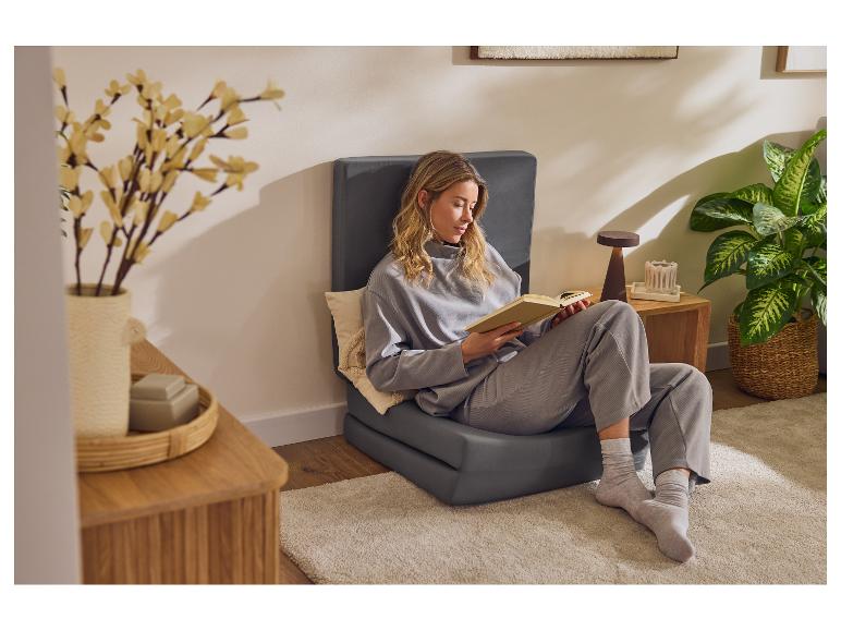 Femme lisant un livre sur un fauteuil de sol gris dans un salon.