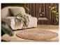 Beige bank met groen kussen en deken, ronde jute vloerkleed op houten vloer.