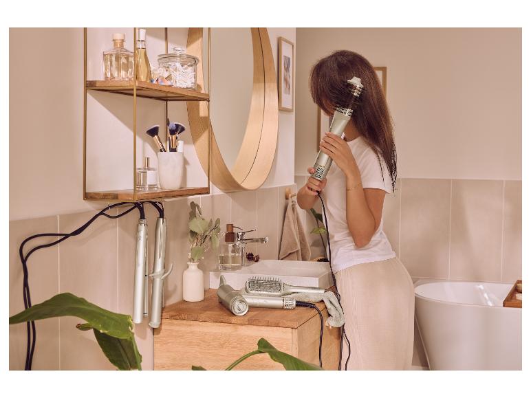Vrouw stylet haar met een warme borstel in een moderne badkamer met haarstylingtools en cosmetica.