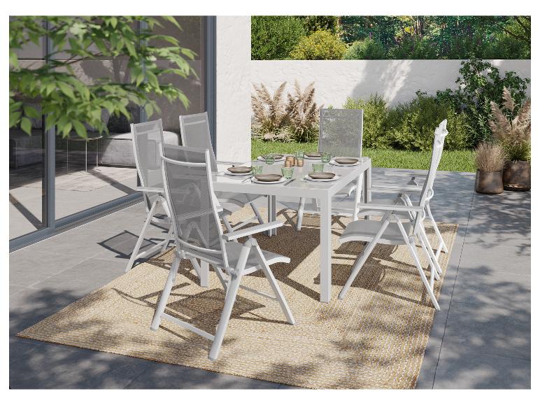 Buiten eethoek met witte tafel en stoelen op een geweven vloerkleed, omringd door groen.