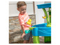 Een kind speelt met water en zand in een speeltafel met een waterbaan.