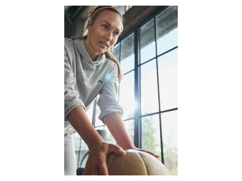 Femme en sweat à capuche gris avec ballon d'exercice.