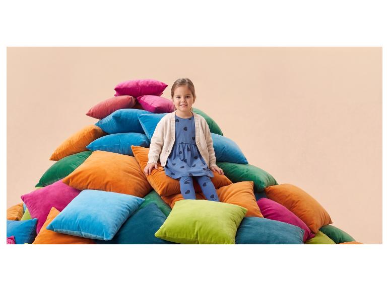 Fille souriante assise sur une pile de coussins colorés.