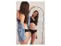 Vrouw in zwarte bralette en slip, met spijkerjack, kijkt in een spiegel.