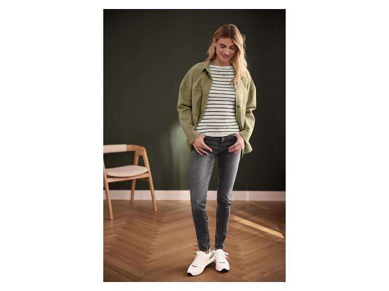 Femme portant une veste verte, un haut rayé, un jean gris et des baskets blanches.