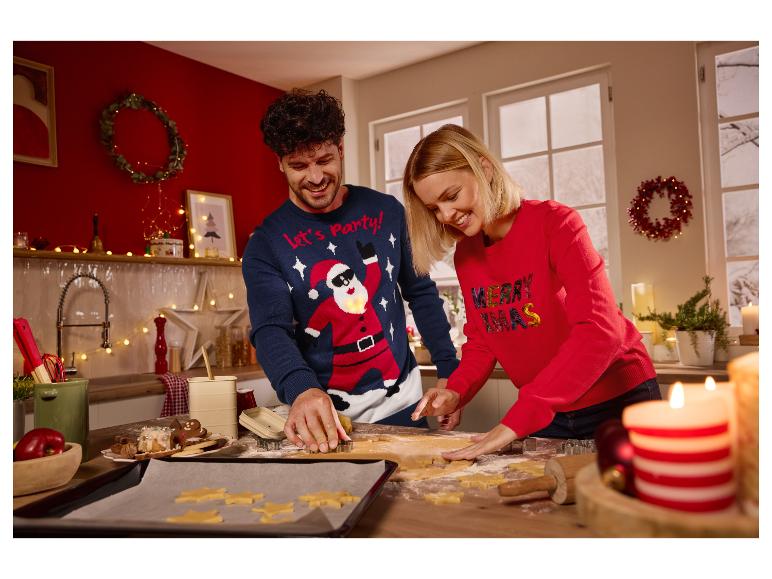 Un couple souriant porte des pulls de Noël et découpe des biscuits dans la cuisine.