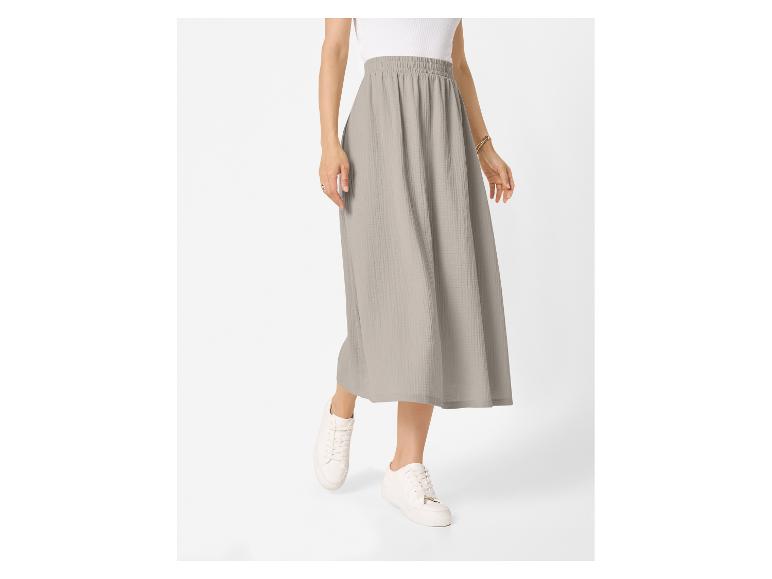Vrouw draagt een lichtgrijze midirok met een witte top en witte sneakers.