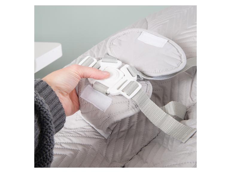 Main attachant la boucle d'un siège bébé ou transat rembourré gris.