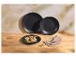 Assiettes noires avec crêpes aux fruits, couverts dorés et serviette sur bois.