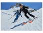 Twee skiërs in zwarte en blauwe ski-uitrusting op een zonnige skipiste.