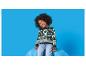 Un enfant souriant aux cheveux bouclés, portant un pull vert à motif de rennes, assis sur une chaise bleue.