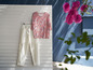 Een wit broek en een bloemetjes blouse hangen aan een witte muur.