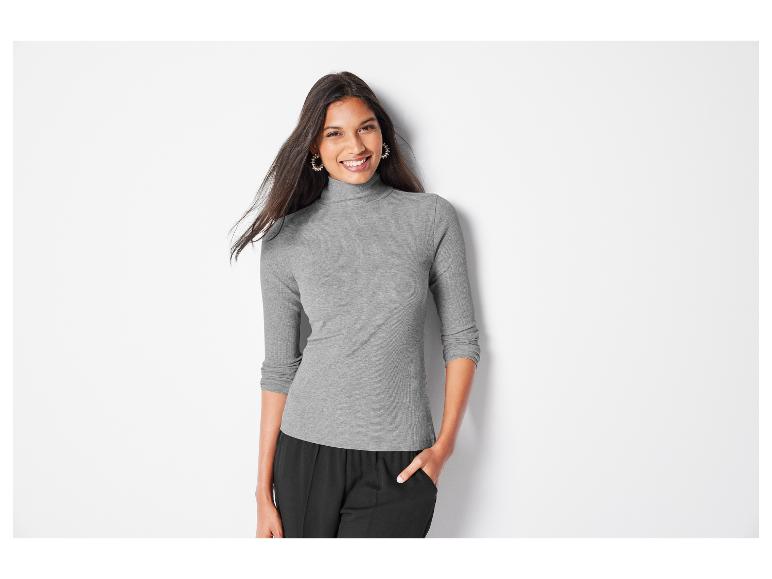 Une femme portant un pull gris à col roulé et un pantalon noir.