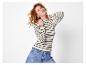 Vrouw met rood krullend haar, gestreepte trui en jeans.