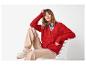 Vrouw in rood vest, beige broek en sneakers, zittend op een witte stoel.