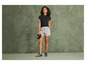 Een vrouw in een zwarte t-shirt en grijze shorts, met een verrekijker in haar hand.
