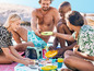 Een groep mensen geniet van een picknick op het strand met een koelbox en kleurrijke servies.