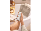 Femme s'épilant la jambe dans une salle de bain, avec baignoire et articles de toilette en arrière-plan.