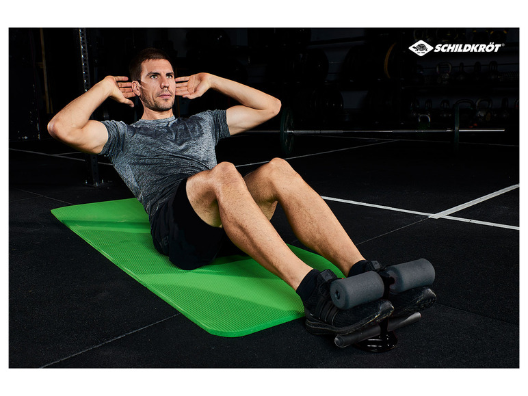 Man doet sit-ups op een groene mat met Schildkröt fitness apparatuur.