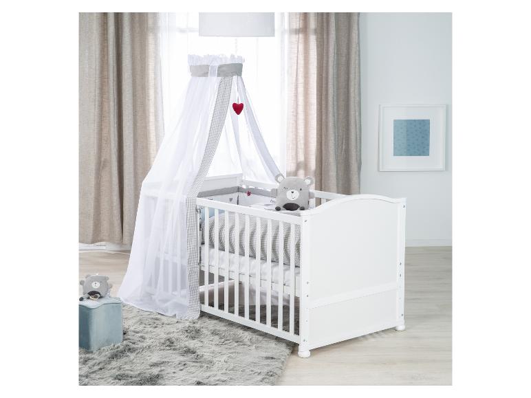 Lit bébé blanc avec baldaquin, ours en peluche gris et tapis dans une chambre d'enfant.