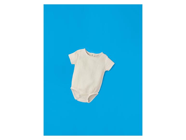 Beige babyromper met korte mouwen op een blauwe achtergrond.