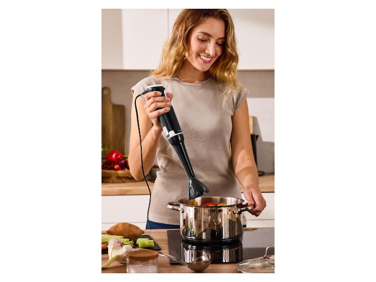 Femme utilisant un mixeur plongeant dans une casserole de légumes sur une plaque de cuisson.