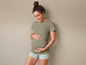 Een zwangere vrouw draagt een groene T-shirt en gestreepte shorts.