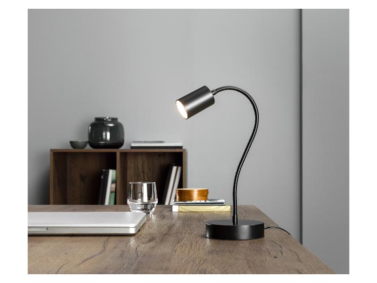 Een zwarte flexibele bureaulamp op een houten bureau met een laptop.