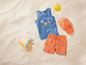 Un débardeur bleu avec un motif de poissons, un short orange à imprimé et une casquette orange dans le sable.