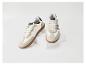 Une paire de baskets crème avec des semelles marron et des détails bleu foncé, présentées sur des boîtes blanches.