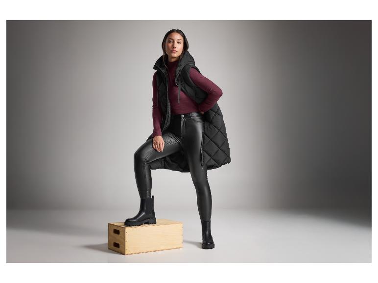 Vrouw in een zwart gewatteerd vest, bordeauxrode trui en zwarte laarzen.