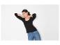 Vrouw in een zwart shirt met lange mouwen en jeans, poserend tegen een witte achtergrond.