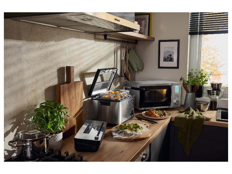 Keuken met friteuse, magnetron, vacuümsealer en pannen op een houten aanrecht.