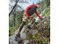 Femme en veste rouge et pantalon à imprimé floral marchant sur des rochers.