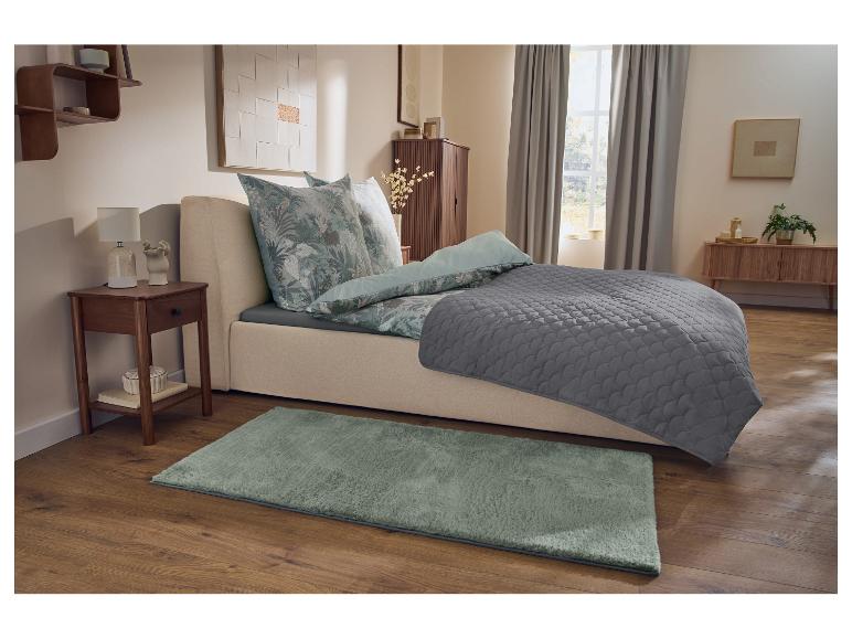 Chambre avec lit, parure de lit à motifs floraux, jeté de lit gris, table de chevet et tapis vert.