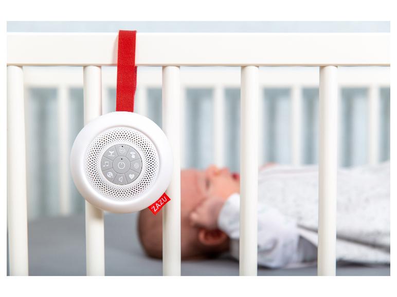 Machine à sons blanche ZAZU accrochée à un lit de bébé avec un bébé endormi en arrière-plan.