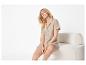 Vrouw in beige overhemd met korte mouwen en korte broek, zittend op een witte stoel.