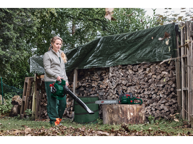 Vrouw met Parkside bladblazer en kettingzaag bij een houtstapel.