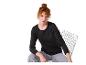 Femme en t-shirt noir à manches longues et jean gris, assise sur une chaise en fil de fer.
