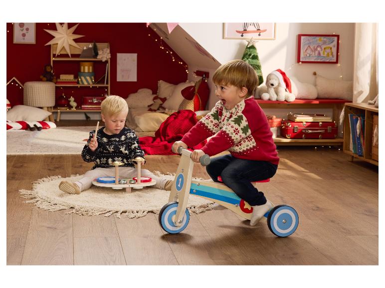 Twee kinderen spelen met kerstspeelgoed in een feestelijk versierde kamer.