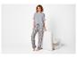 Vrouw in grijze pyjama met paisley-patroon, poserend naast een witte stoel.