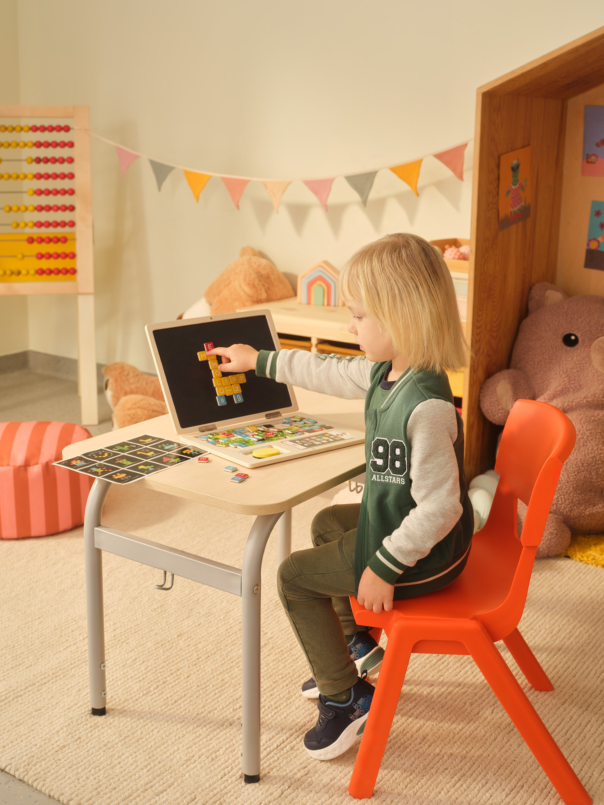 Kind speelt met een houten laptop en magneetletters aan een klein bureau.