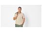 Man in beige poloshirt en groene korte broek, met groen jasje over schouder.