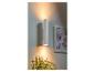 Un luminaire mural cylindrique blanc éclaire une pièce avec une plante et un tableau.